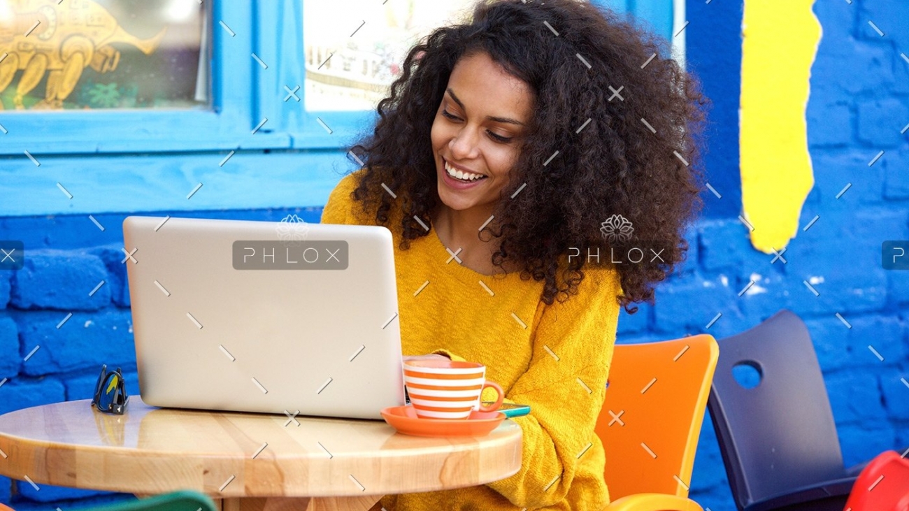 happy-young-woman-sitting-at-outdoor-cafe-using-PFFBJ93